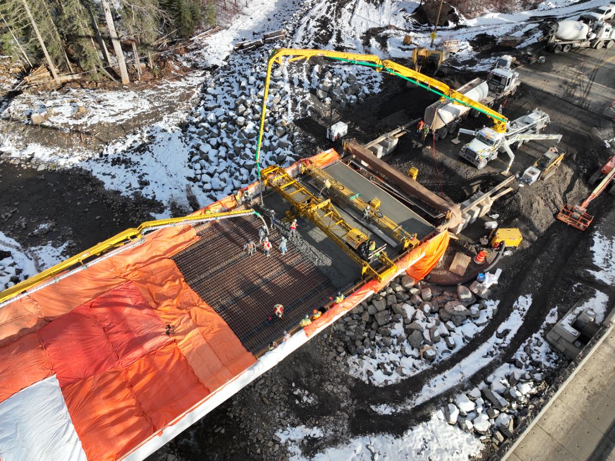 Aerial view of a bridge deck concrete pour with a pump truck and orange hoarding in snow