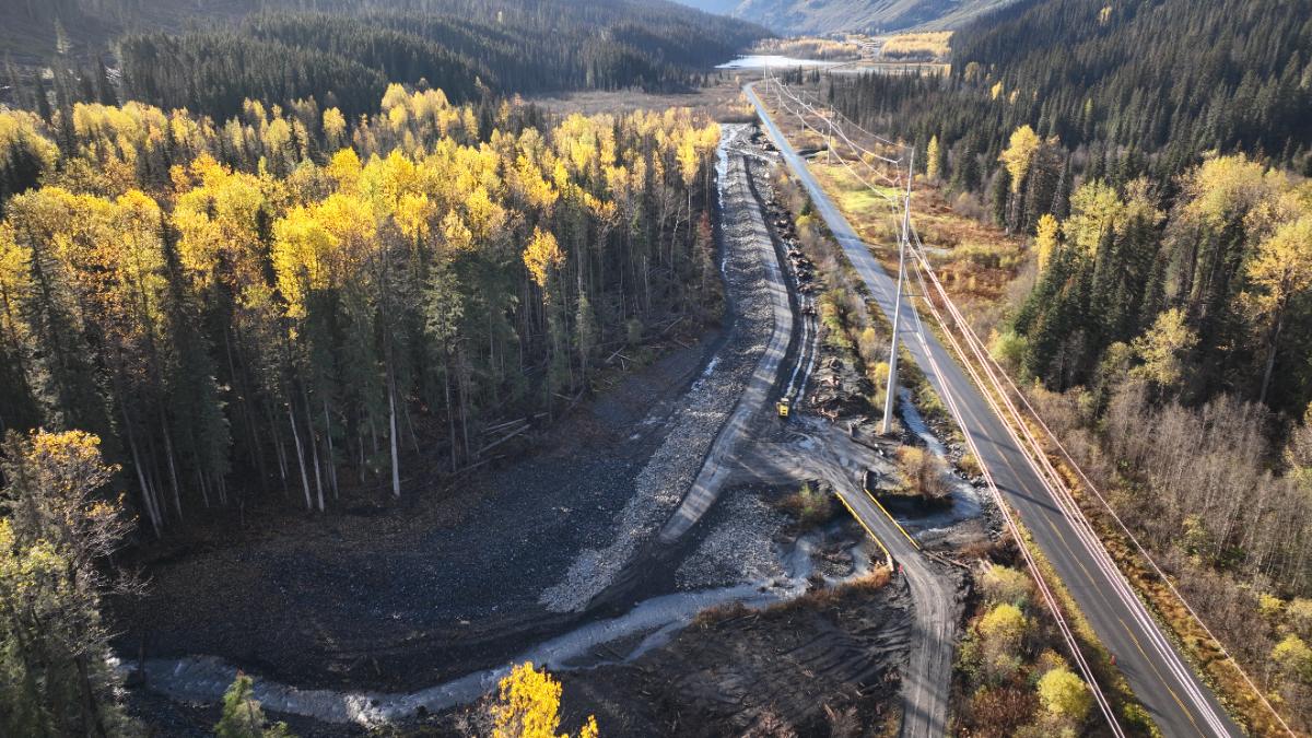 Aerial view of a rebuilt creek channel and rock armour beside a mountain highway in autumn
