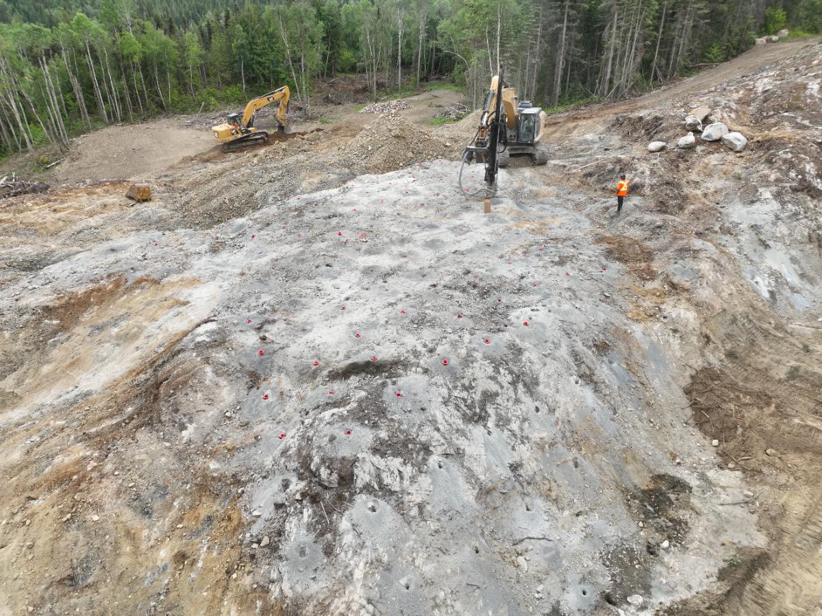 Rock face drilled out on a grid pattern with a drill rig and excavator, ready for blasting