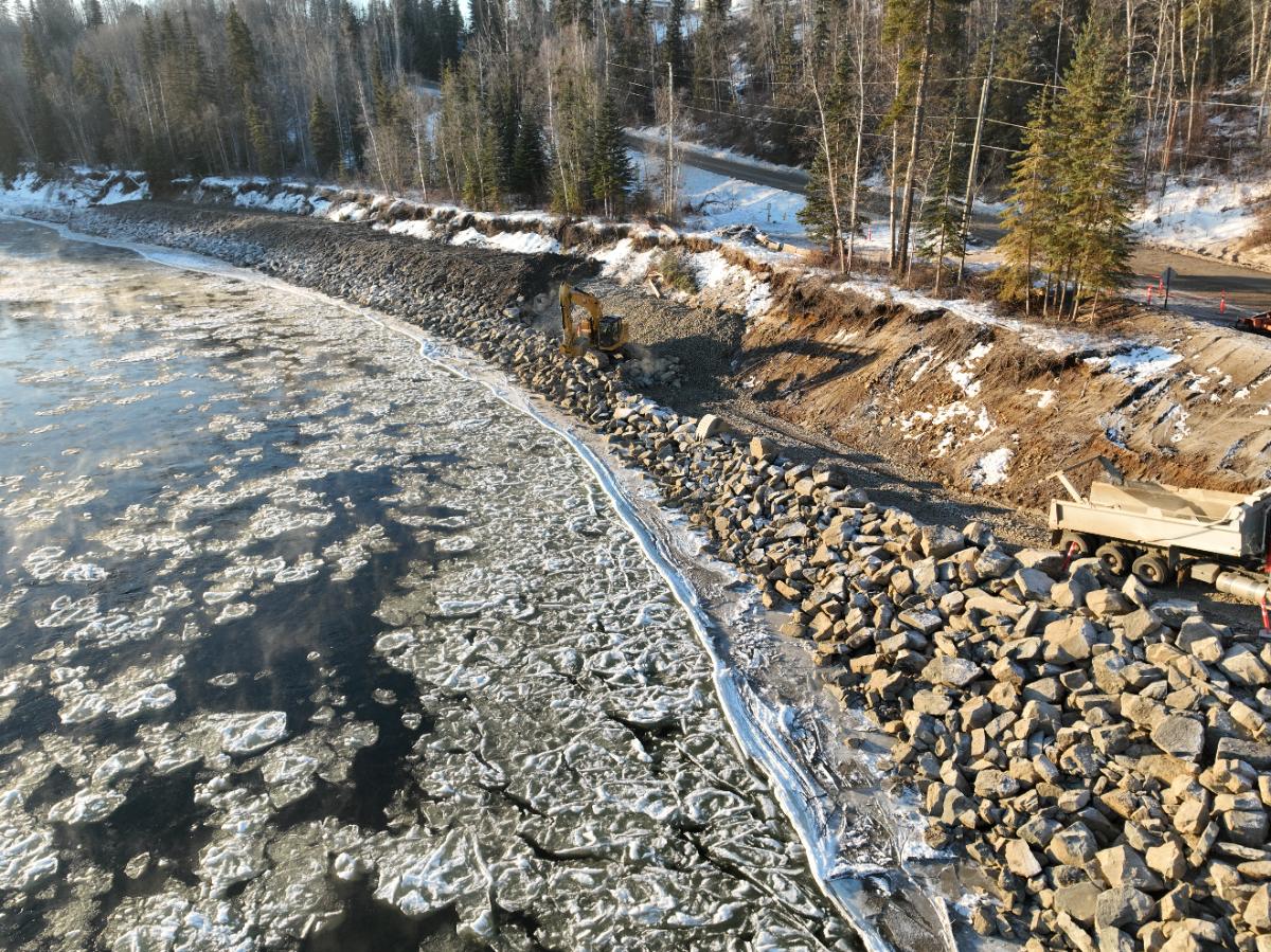Excavator placing riprap along a frozen riverbank in winter